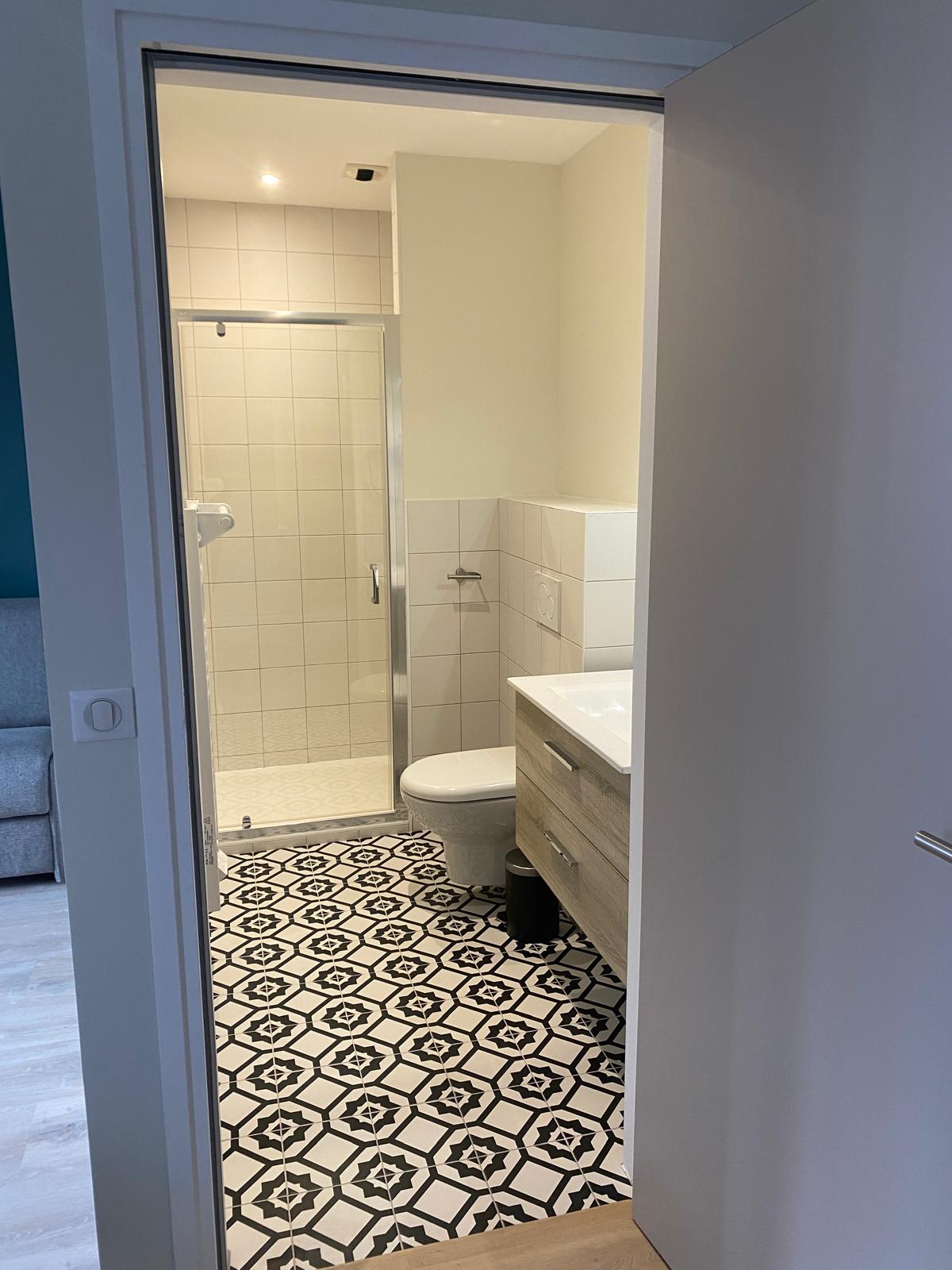 Salle d'eau rénovée avec douche, faïence blanche et sol carrelé à motifs